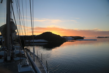 widok z jachtu na spokojne zimne wody oraz górzyste i ośnieżone wybrzeże antarktydyo zachodzie słońca © KOLA  STUDIO