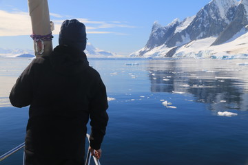 człowiek z tyłu stojący na jachcie i patrzący na piękne górzyste ośnieżone wybrzeże antarktydy - obrazy, fototapety, plakaty