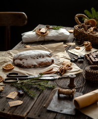 Fototapeta na wymiar tasty homemade traditional christmas dessert stollen with dried berries and nuts on parchment in woman hand on wooden rustic table with spices, orange slices, Christmas tree branches, selective focus