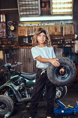Plakat Nice small girl is posing for photographer with big wheel from car at auto service.