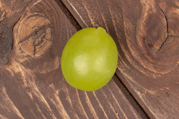 One whole fresh green grape flatlay on brown wood