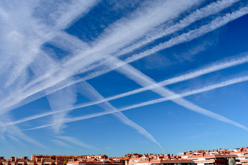 Many chemtrails or contrails produced by airplanes flying on blue sky over the city. conspiracy...
