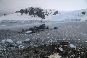 czerwony ponton przycumowany do skalistego brzegu w zimnej zatoce pokrytekj krą i ośnieżone góry w tle