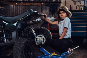 Fototapeta na wymiar Serious beautiful girl want to be an auto technician when she grows up, she is trying to fix broken ATV.