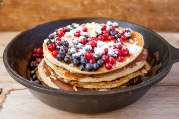 Stack of homemade shrovetide carnival clean eating oat pancakes with powered sugar, blueberries and cowberries in cast iron pan on rustic country table. Soft focus. Copy space