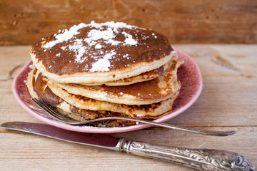 Stack of homemade clean eating oat pancakes with powered sugar on pink plate on rustic country table with old silver tableware. Selective soft focus. Shrovetide, pancake carnival maslenitsa concept