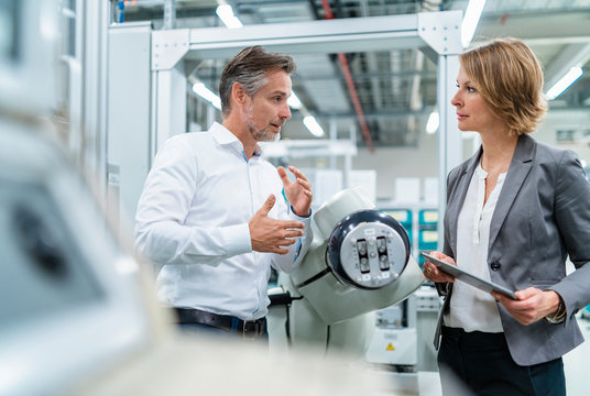 Businesswoman and man talking at assembly robot in a factory