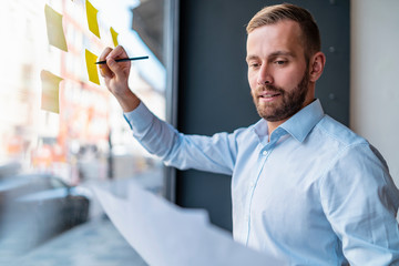 Businessman writing on adhesive notes at glass pane