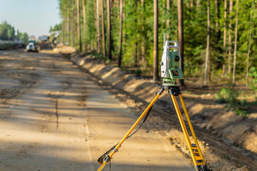 Surveyor engineer with equipment (theodolite or total positioning station) on the construction site of the road or building with construction machinery background