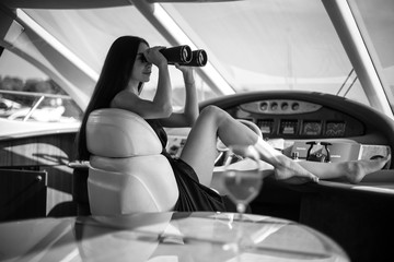 Young beautiful woman in a long silk black dress posing on a yacht. Luxurious life style, summer time