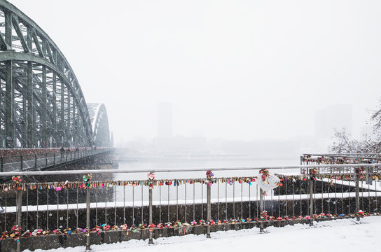 Padlocks on railing by Hohenzollern Bridge over Rhine river against sky during snowfall