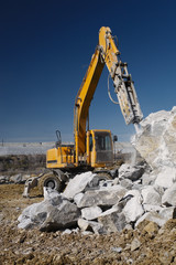 Hydraulic breaker hammer destroys a large stone against the background of a blue sky, close-up, front view. Heavy equipment. Mining industry.