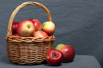Wicker basket with ripe juicy apples. Nearby are a few apples. New crop. On a gray background.