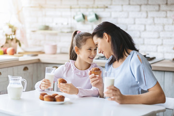 Mother and daughter eating cupcakes and drinking milk in kitchen.