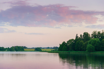 Fototapeta na wymiar Lake landscape reflects the distant green shore of trees sunset warm purple pink blue sky and delicate stacked clouds, water, nature