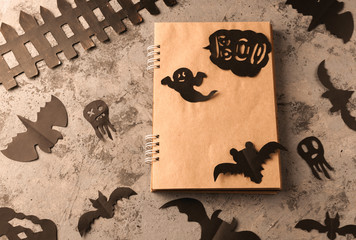 Figures from a black bat and ghosts carved from black paper on a concrete surface. Notepad with craft sheets and copy space. Crafts for halloween celebration concept. Handwork. Flat lay