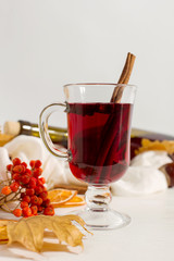 A cup of mulled wine with spices, bottle, scarf, spices, dry leaves and oranges on the table. Autumn mood, method to keep warm in cold, copy space.