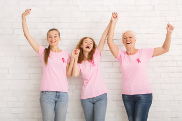 Three Women Wearing Breast Cancer T-Shirts Holding Hands Against Wall