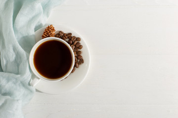 Blue scarf, coffee grains and a cup on a white table, morning start day. Autumn mood background, copy space, flat lay.