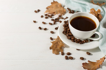 Dry yellow leaves, blue scarf, coffee grains and a cup on a white table, morning start day. Autumn mood background, copy space, flat lay.