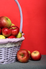 Wicker basket with ripe juicy apples. Nearby are a few apples. New crop. On a coral background.