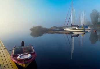 Autumnal mist on a river with sailboats and fishing boats anchored in harbor,  at dawn, Europe