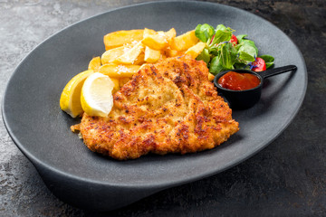 Frittiertes Wiener Schnitzel vom Kalb von der Oberschale mit Pommes Frites und Salat als closeup auf einem Modern Design Teller