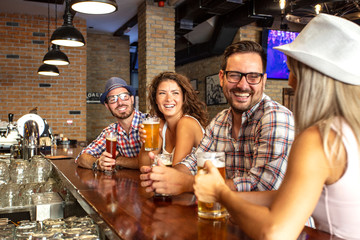 Two couples in beer house sitting with full glasses of beer in front and chat