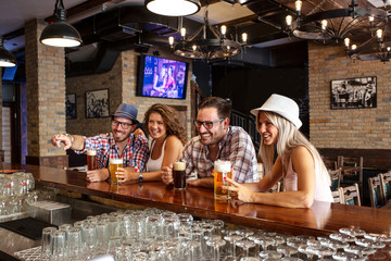 Two couples in beer house sitting with full glasses of beer in front and chat