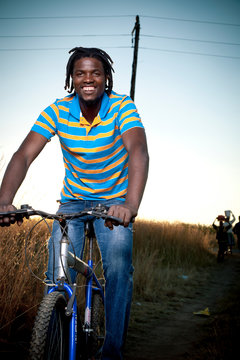 Young black adult male rides a bicycle through the streets while smiling at camera