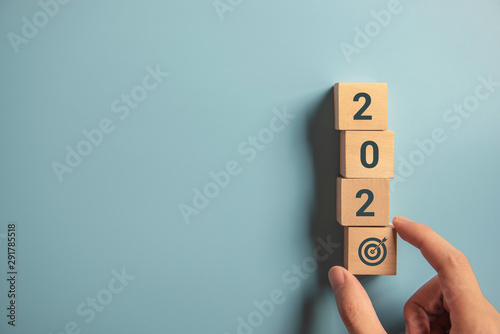 Hand holding wood wooden cubes with New year 2020 and goal icon concept.
