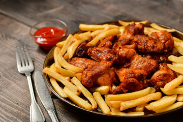 Hot chicken wings and french fries with ketchup and mustard. food lunch or dinner, typical fast food. on a wooden background. food delivery concept.