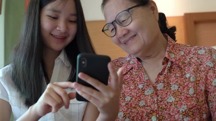 Asian pretty niece teaching her grandmother to using smartphone and new technology feeling happy and smiling, family concept