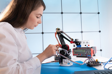 A young woman writes an algorithm for the robot arm. Science Research Laboratory for Robotic Arm Model. Computer Laboratory