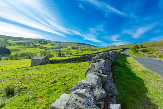 Yorkshire Dales landscape, single track road between Askrigg and Gunnerside with blue sky, white clouds and green fields.  Horizontal.  Space for copy.