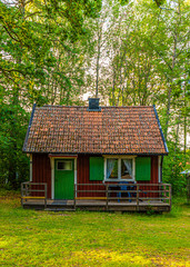 Fototapeta na wymiar Small red, white and green wooden cabin in a forest.