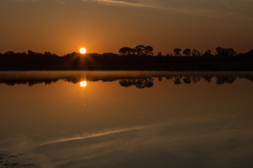 Sunrise at the border of the Netherlands and Belgium. Two countries split by the river Meuse. Picture taken from the belgium side during golden hour with reflection in the water