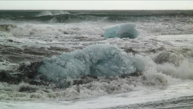 Waves crash over Iceland glacial ice, medium shot