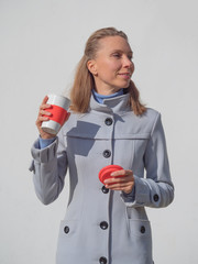 Reusable coffee cup in the hands of a woman in a light coat against a white wall.