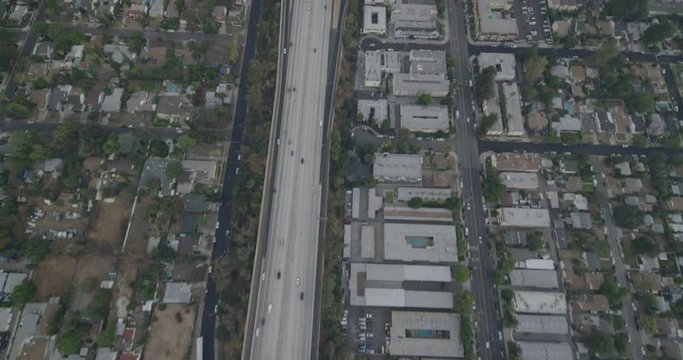 Helicopter aerial tracking speedily down freeway, cars seen moving below, day
