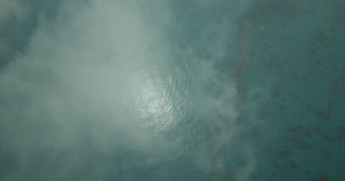 Birds eye view helicopter aerial shot over blue ocean and reef through clouds, day