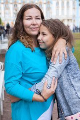 Mother and pre-teen daughter embracing together in summer park, curly hair females