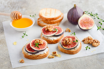 Bruschetta with fresh ricotta cheese, figs, nuts, thyme  and honey on gray concrete background.