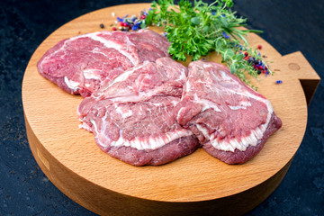 Traditionelle rohe deutsche Ochsenbäckchen angeboten als closeup mit Kräutern und Gewürzen auf einem Modern Design Holz Schneidebrett 