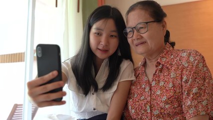 Asian grandmother and her niece having fun with using smartphone and taking selfie together, family concept