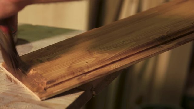 Carpenter is covering wooden plank with lacquer. Workers hand covering wooden panel with finishing protective cover.