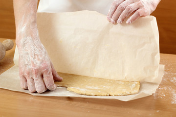 Baker rolling a dough between sheets of baking paper. Making Pastry Dough for Hungarian Cake. Series.