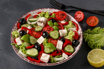 Healthy Greek salad of green lettuce, cherry tomato, onion, pepper, feta cheese, black olives, basil, cucumbers, with olive oil and lemon juice, closeup, horizontal orientation