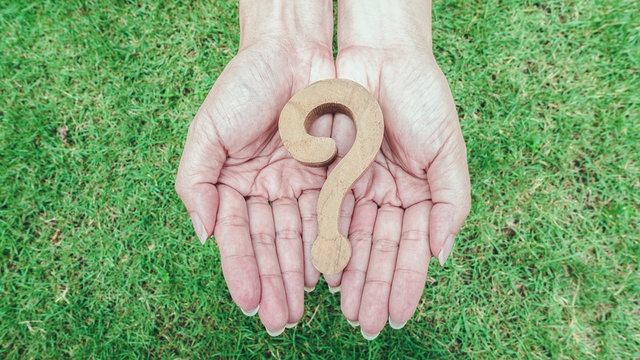 Wooden question marsk on woman hands over green grass background. Ploblem solving concept.