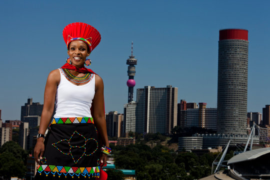 Traditionally dressed African woman stands with cityscape in background